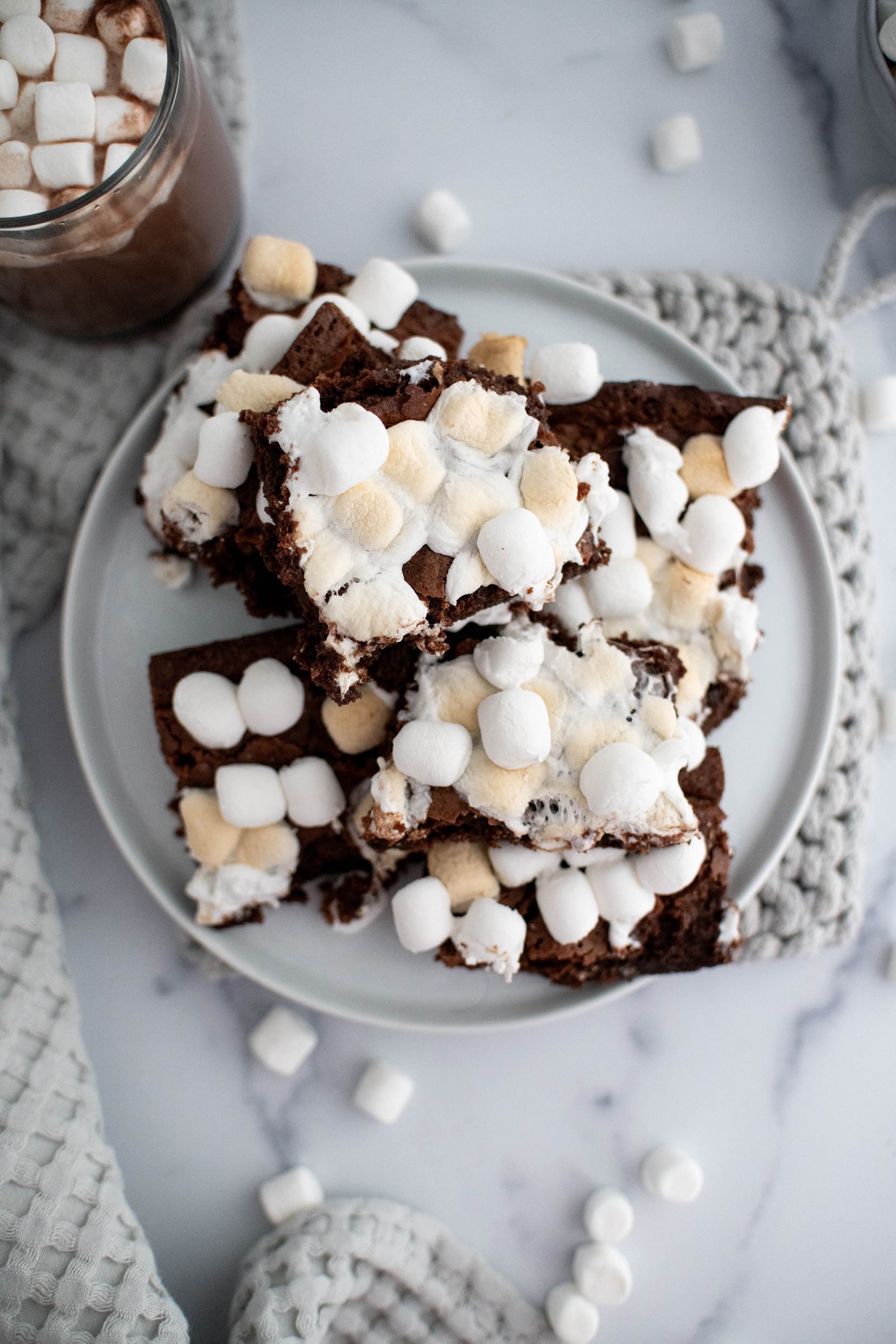 Pile of hot chocolate brownies on a round plate with a mug of hot chocolate to the left of the plate. Waffle weave towel in the forefront.